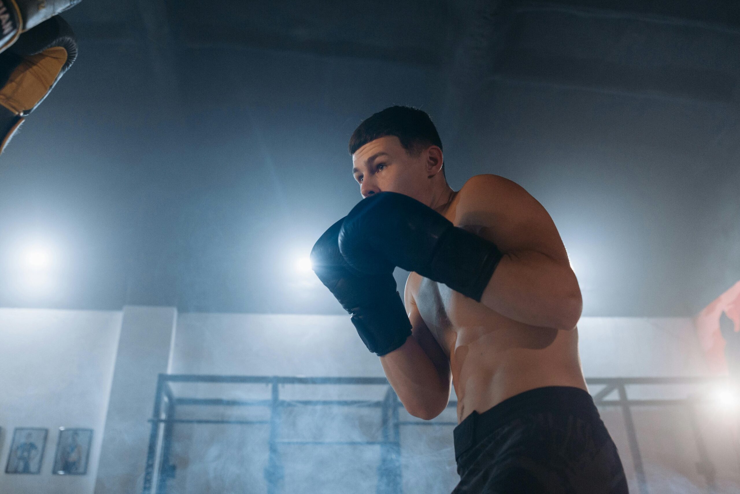 Shirtless man in boxing stance during intense indoor gym training.